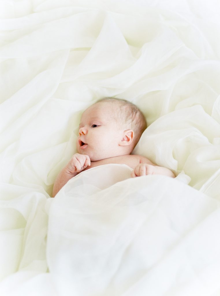 a baby surrounded by flowing sheets laying on a bed