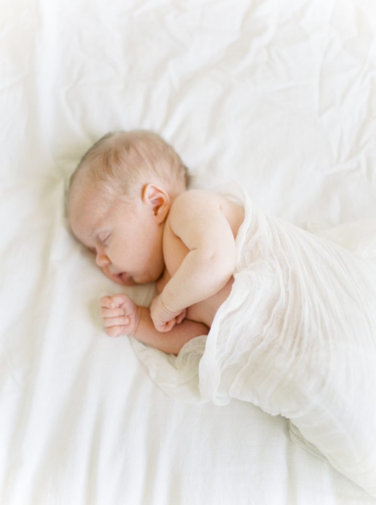 newborn baby is sleeping on his side on a white bed