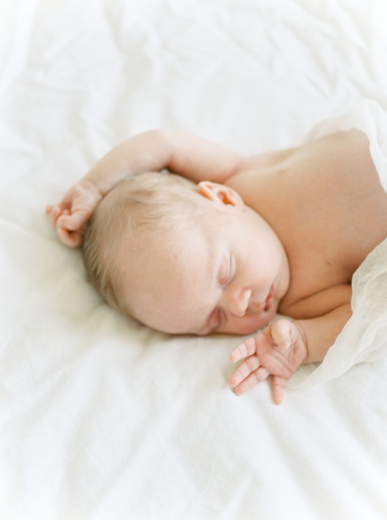 newborn baby asleep with hands by his head