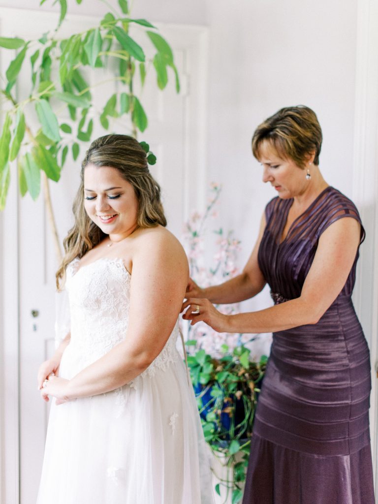 bride's mother helping her zip her wedding dress